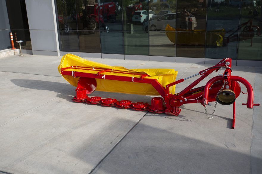 A yellow and red lawn mower is parked on the sidewalk in front of a building.