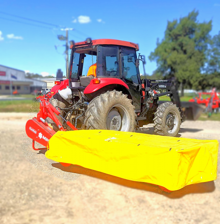 A red tractor with a yellow mower attached to it is parked on a dirt road.