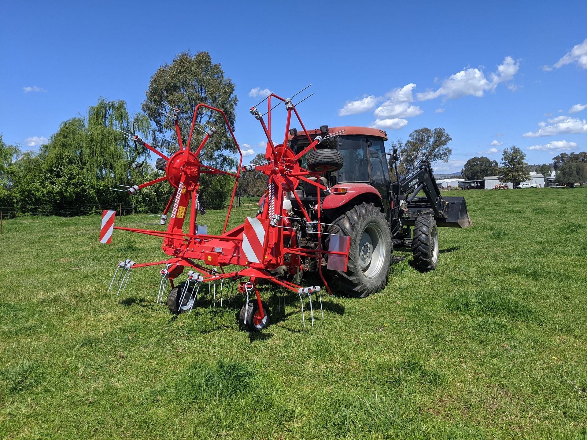 A red tractor is parked in a grassy field next to a hay rake.