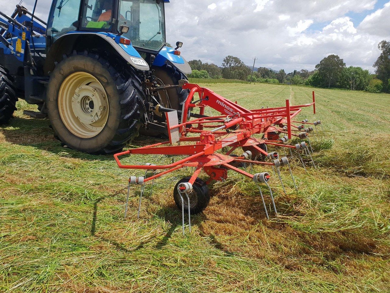 A tractor is driving through a grassy field with a hay rake attached to it.