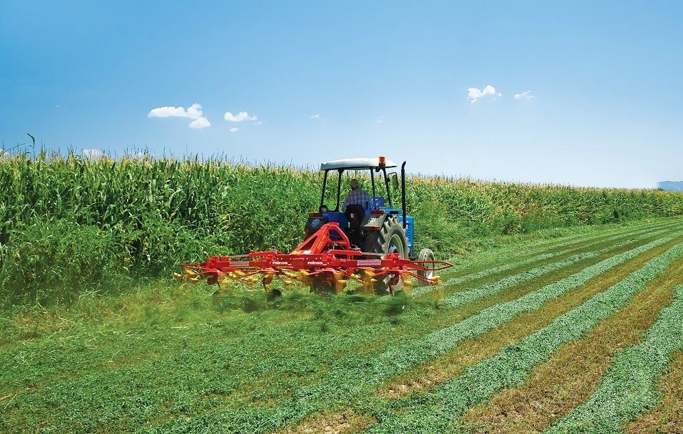 A blue tractor is cutting grass in a field.