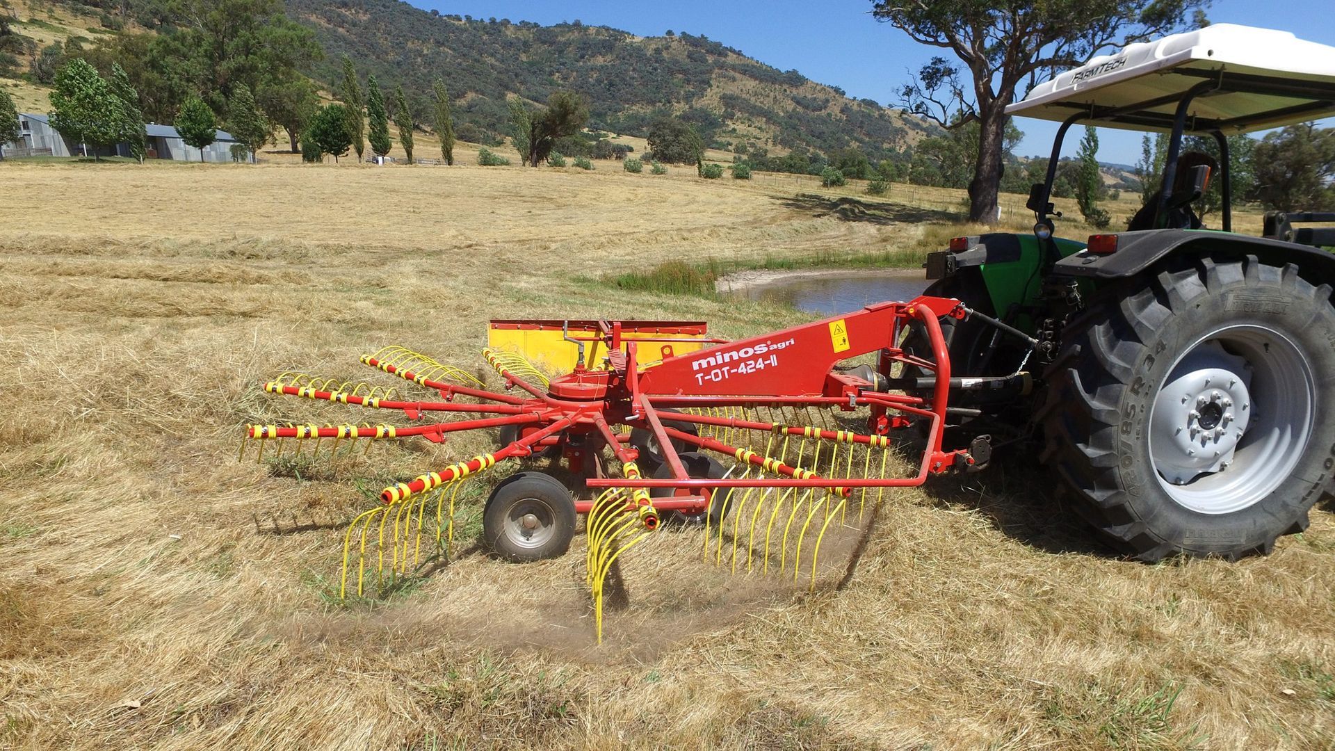 A tractor is in a field with a hay rake attached to it.