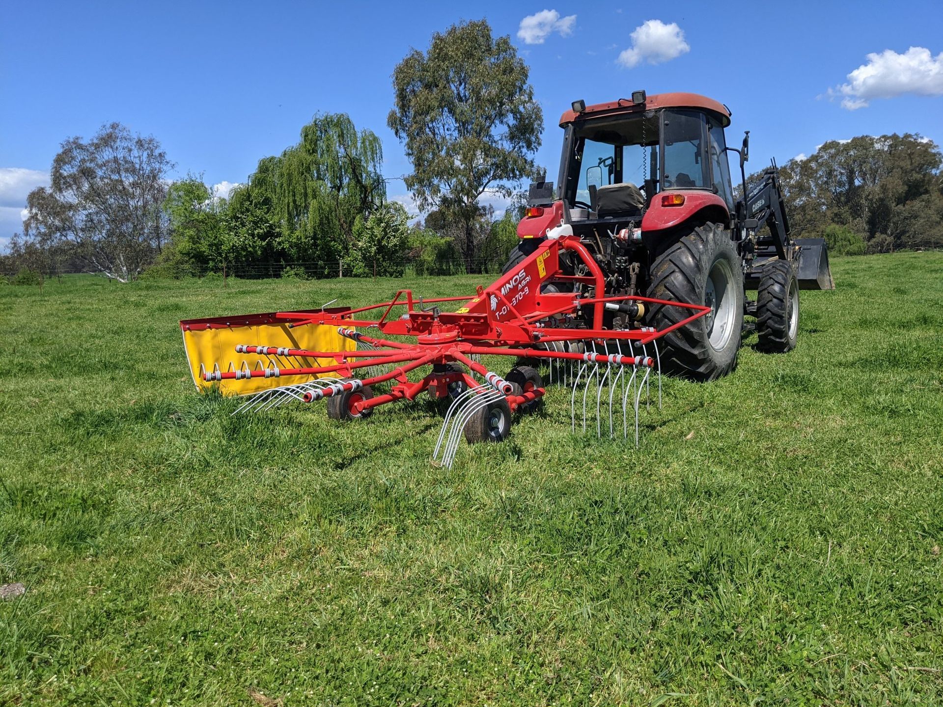 A tractor is driving through a grassy field with a hay rake attached to it.