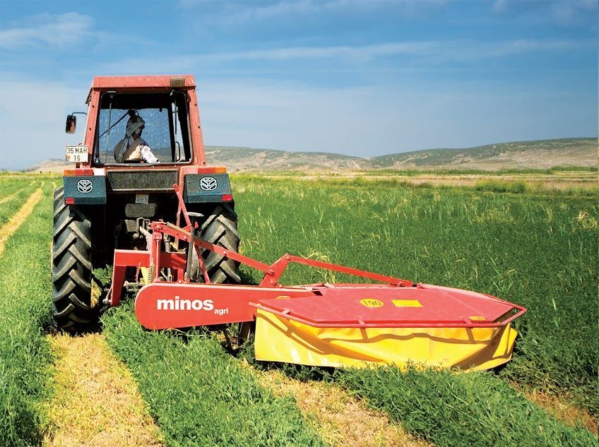 A man is driving a tractor in a field with a minos mower attached to it