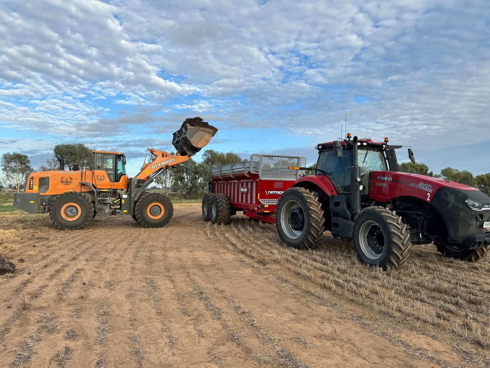 Two tractors are parked next to each other in a dirt field.