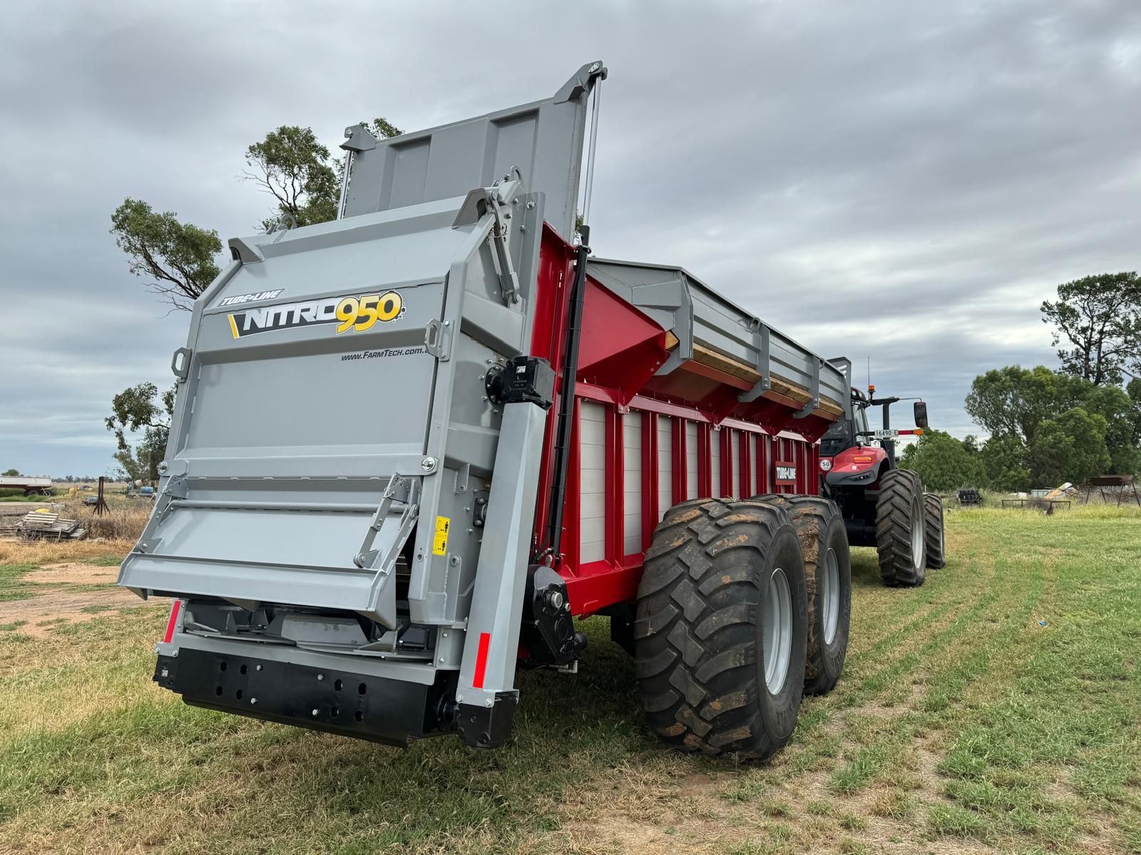 A red tractor is pulling a large dump trailer in a field.