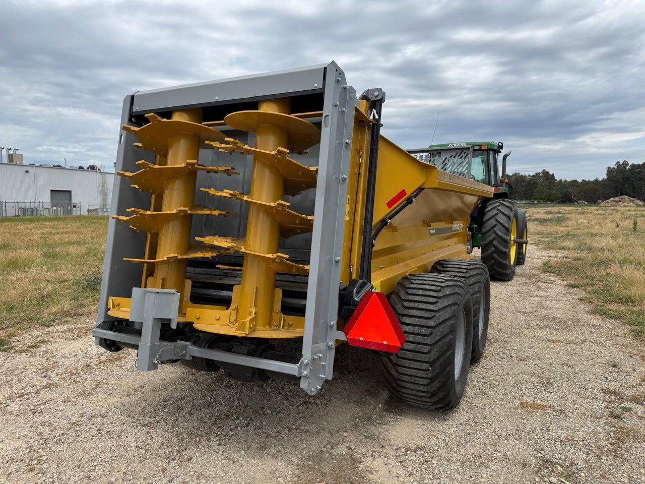 A tractor with a trailer attached to it is driving down a dirt road.