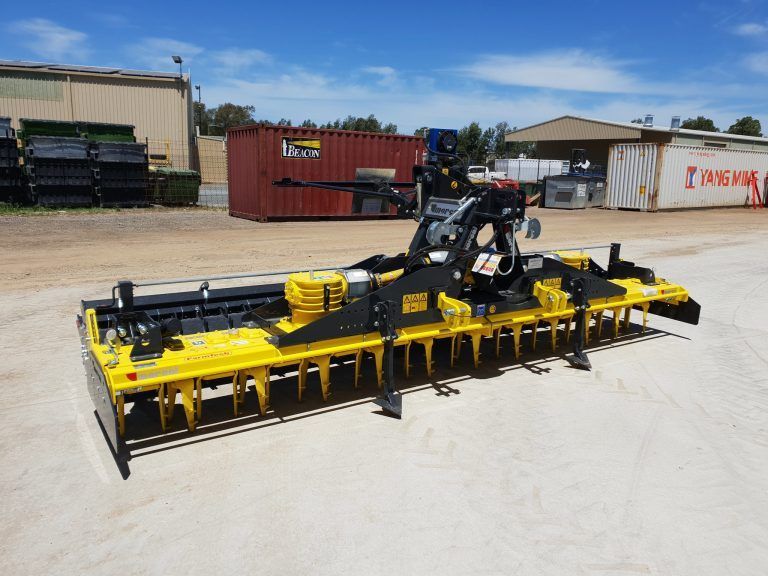 A yellow and black power harrow is parked in a dirt lot