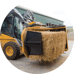 A bulldozer is carrying a bale of hay in its bucket.