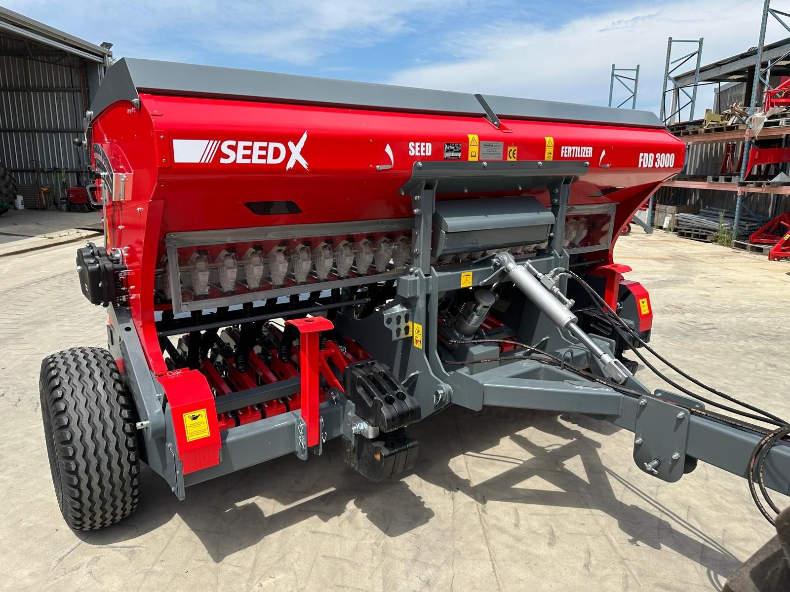 A red and gray seed drill is parked in a parking lot.