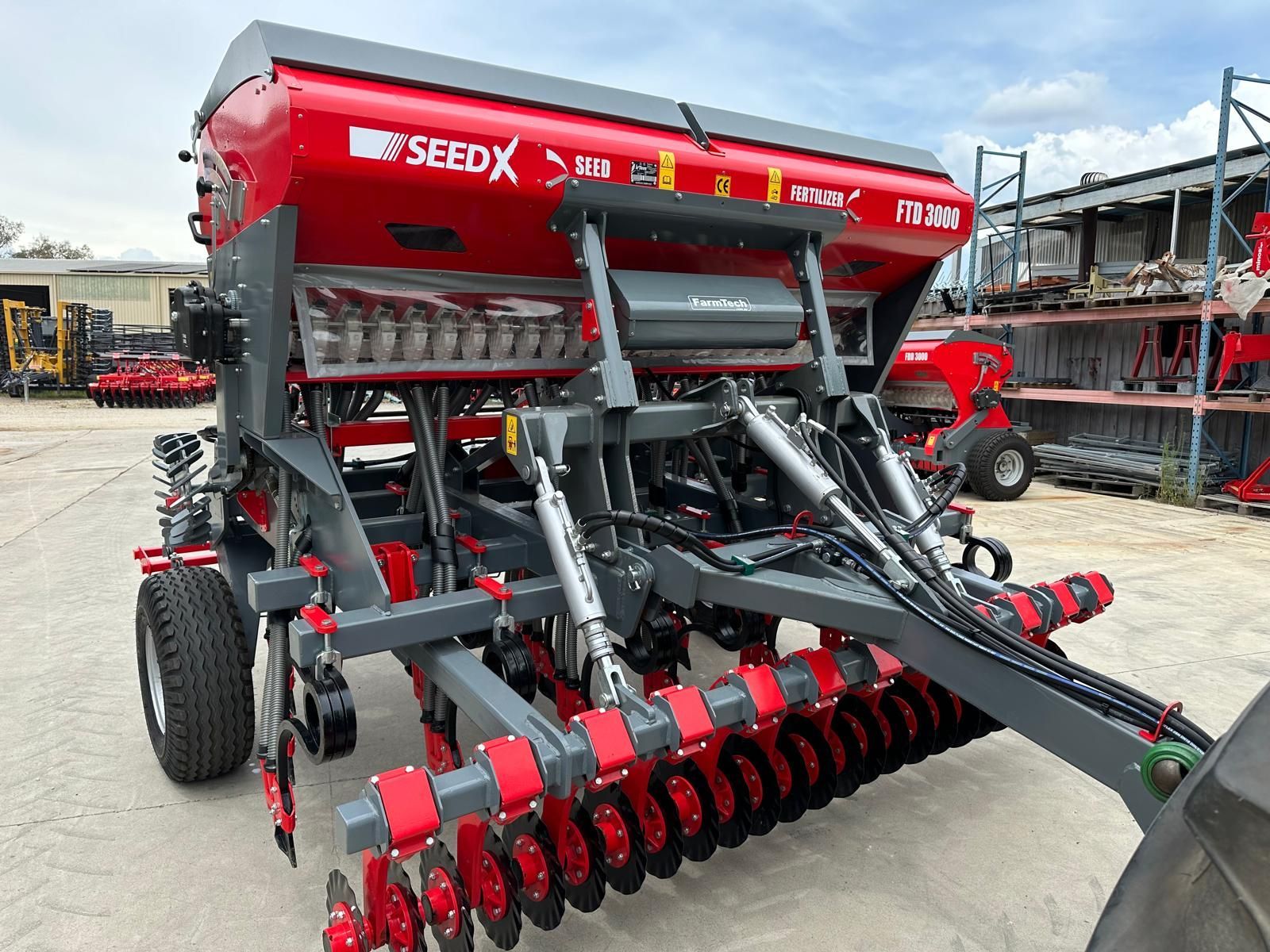A red and gray seed drill is parked in a parking lot.