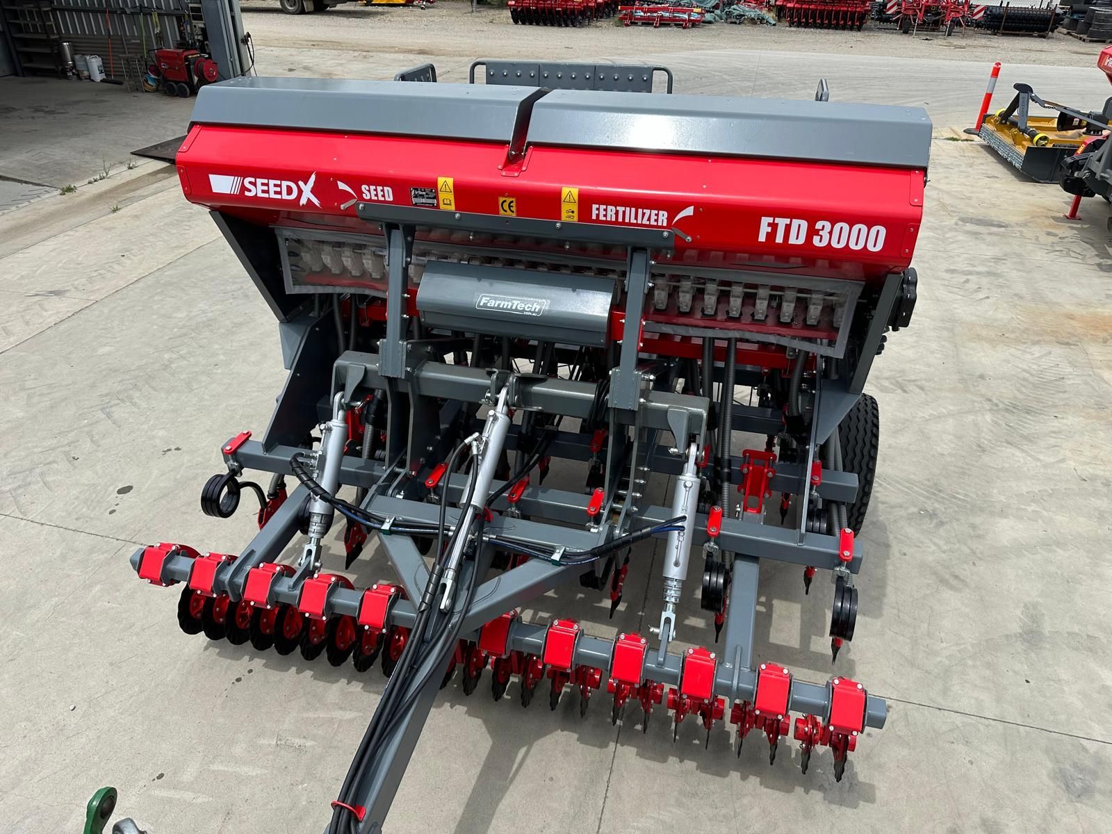A red and gray seed drill is parked in a parking lot.