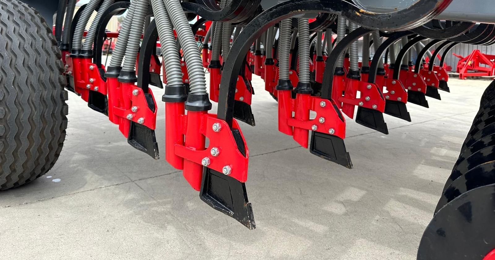 A close up of a seed drill with red and black tines on the ground.