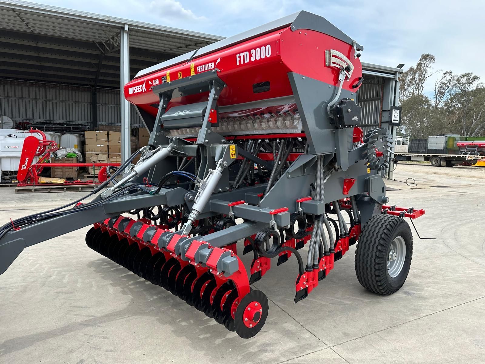 A red and gray seed drill is parked in a parking lot.