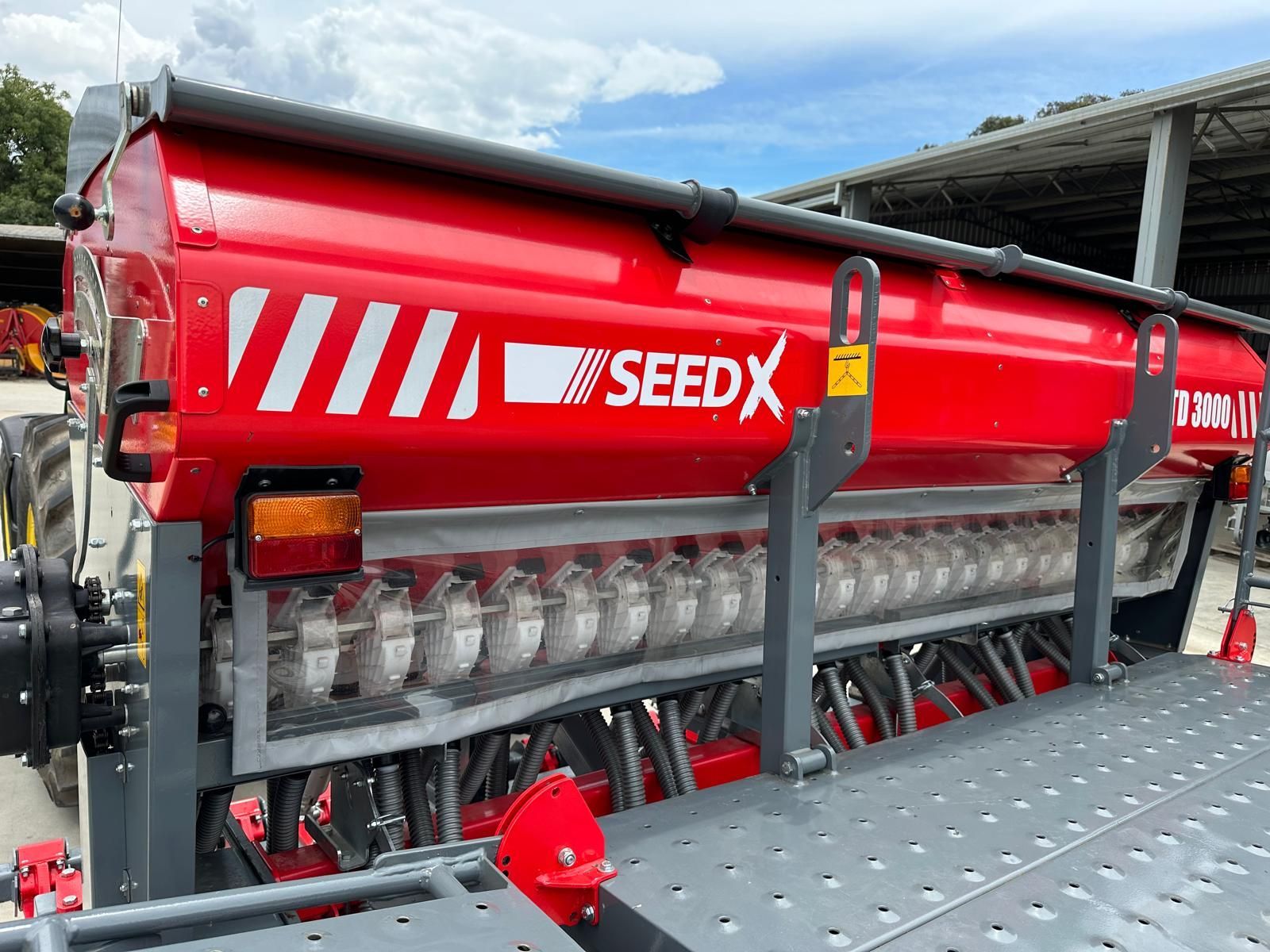 A red and gray seed x seed drill is parked in a parking lot.