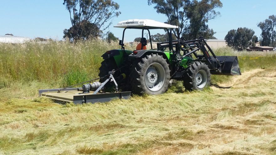 A green tractor is cutting grass in a field