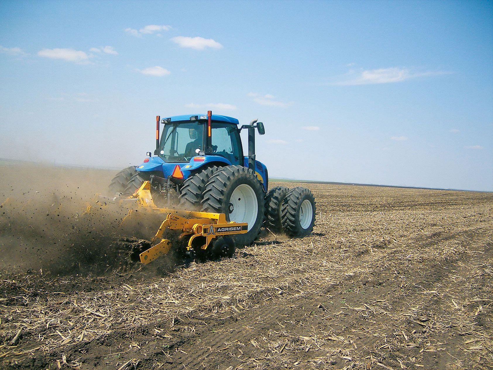 A blue and yellow tractor is plowing a field.