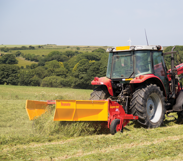 A red tractor is cutting grass in a field