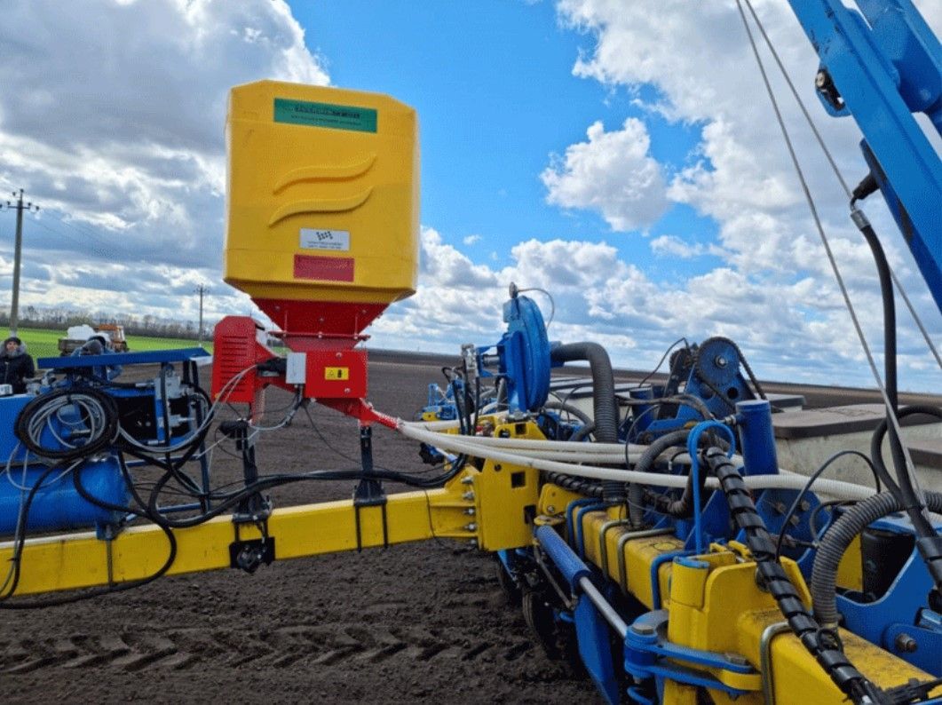 A yellow and blue tractor is sitting on top of a dirt field.