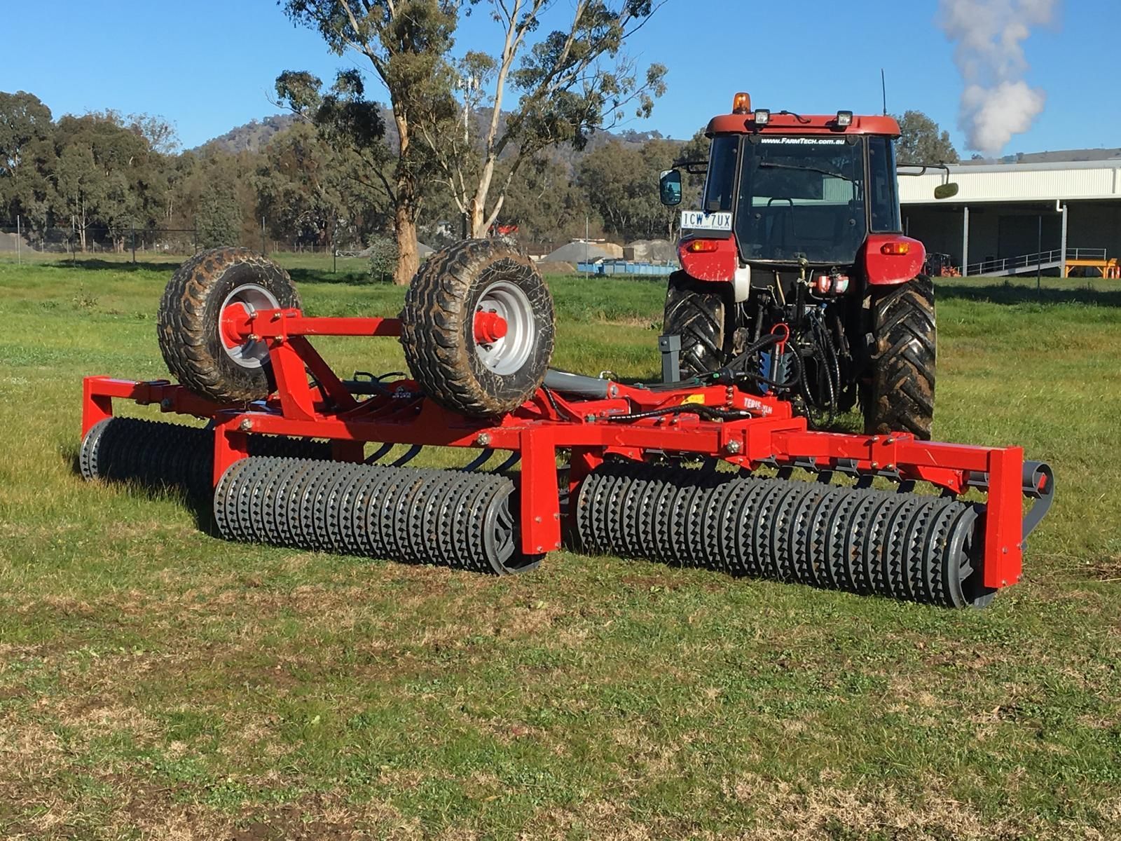 A tractor is plowing a field with a disc tiller attached to it.