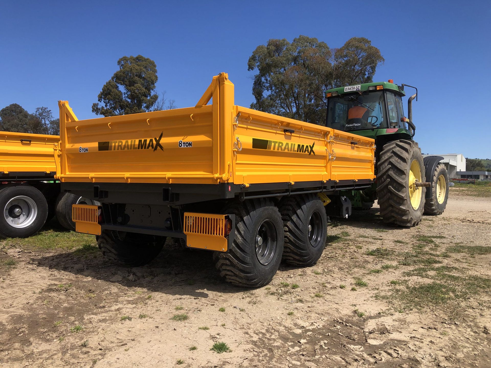A yellow dump truck is parked next to a tractor in a dirt field.