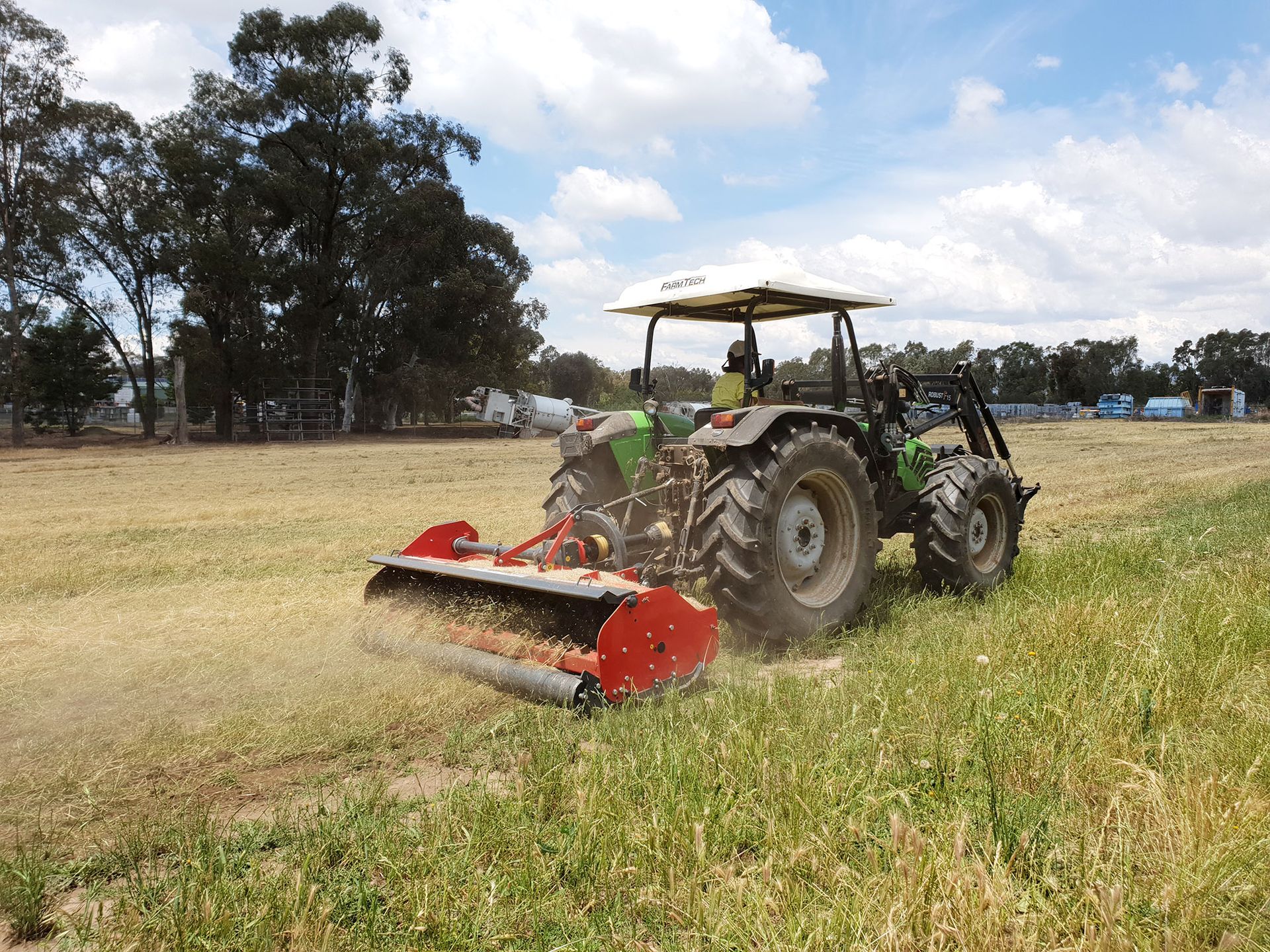 A blue tractor is cutting grass in a field.