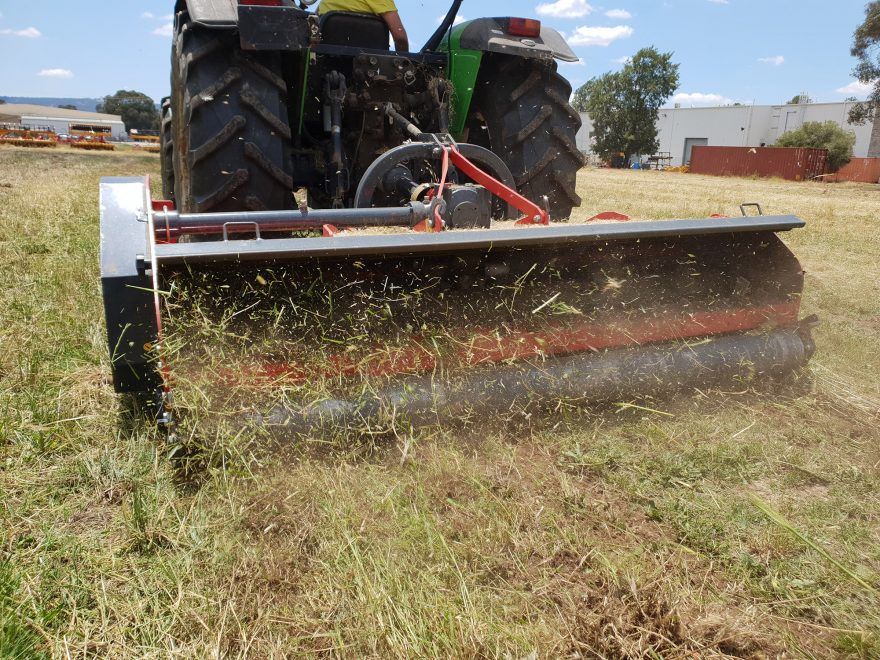 A tractor is cutting grass in a field with trees in the background