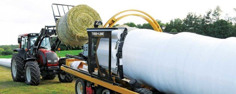 A tractor is wrapping a bale of hay in a plastic bag.