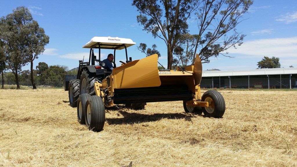 A man is driving a tractor in a field towing a hay conditioner.