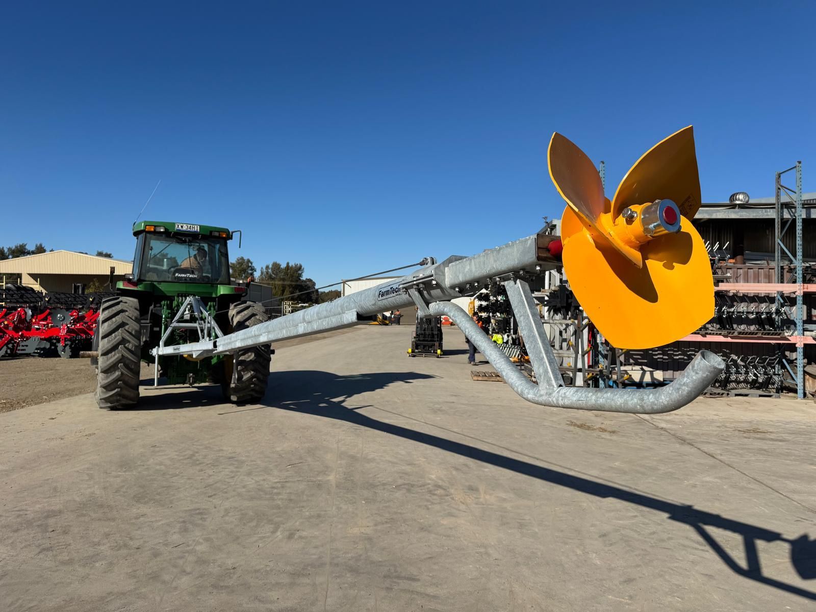 A red tractor is pumping dirt into a large tank