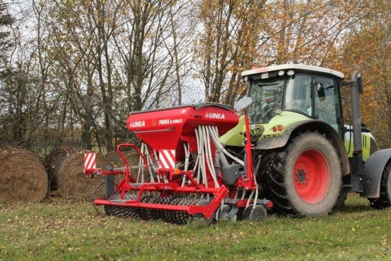 A tractor is plowing a field with hay bales in the background.