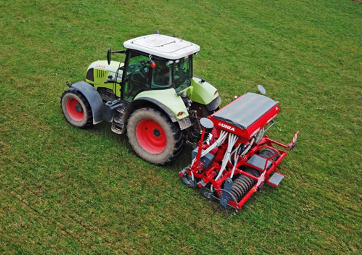 A tractor is driving through a grassy field with a machine attached to it.