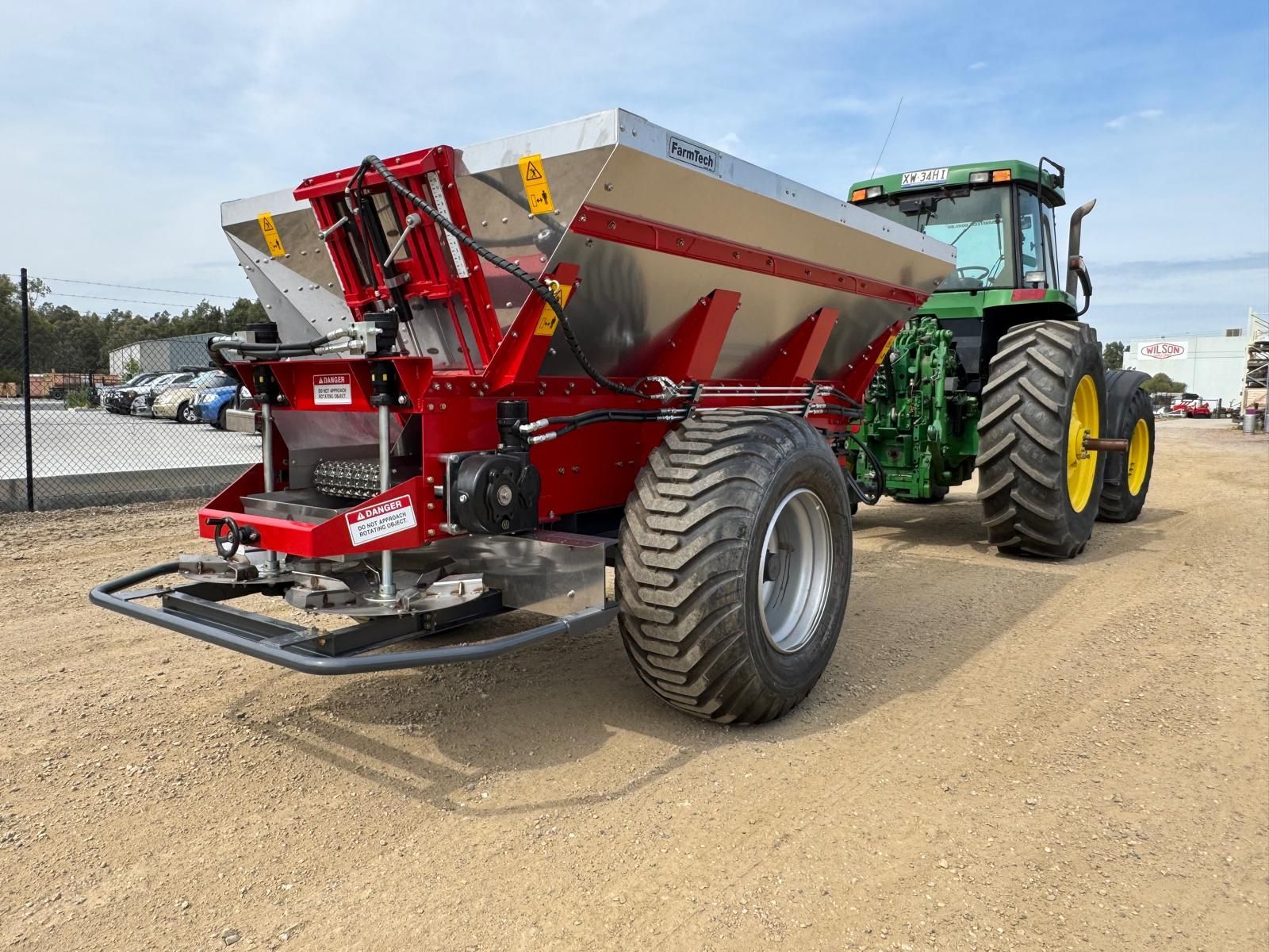 A tractor is parked in a grassy field with a spreader attached to it.