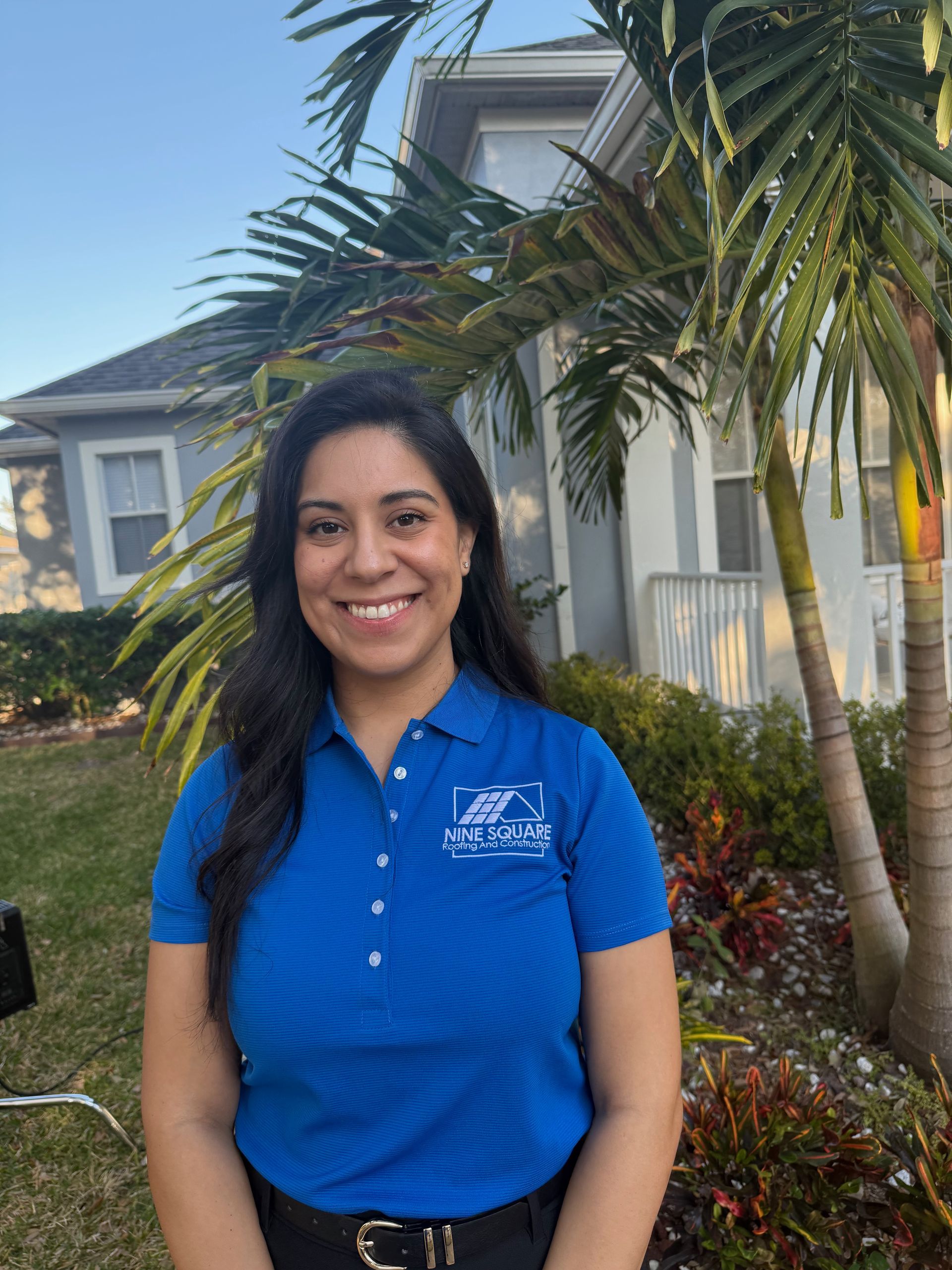 Woman in blue polo smiling in front of a house with a palm tree.