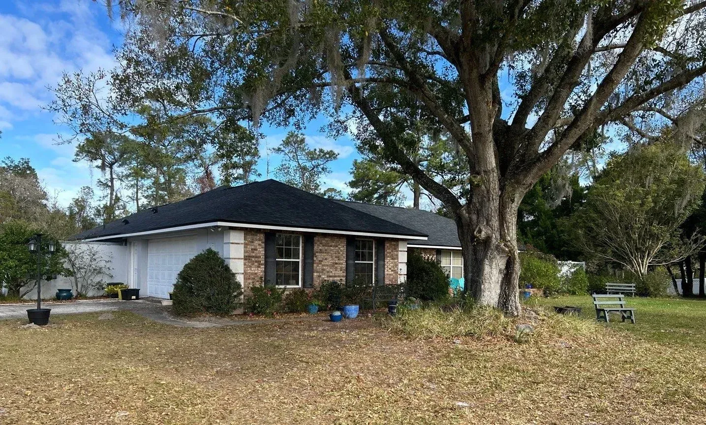 A house with a black roof and a tree in front of it.