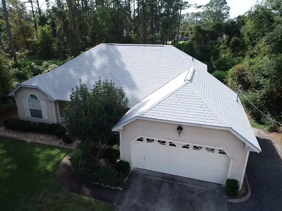 An aerial view of a house with a white roof and a garage.