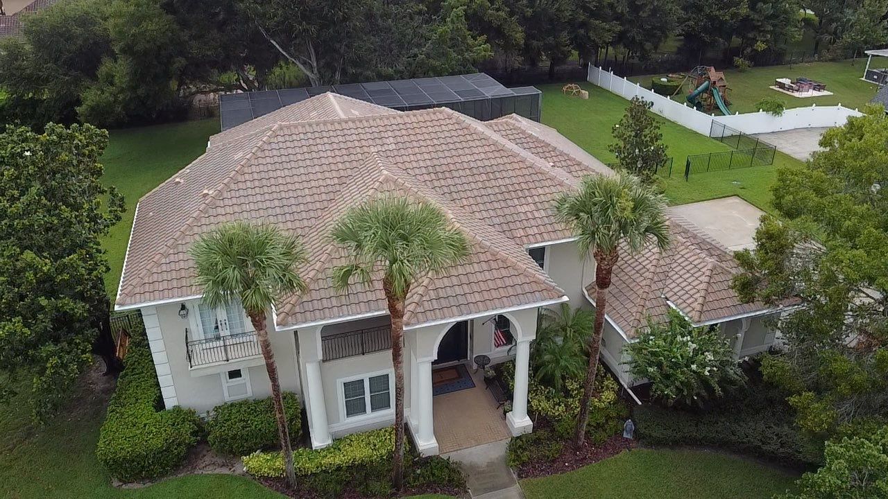 An aerial view of a white house with a brown roof and palm trees.