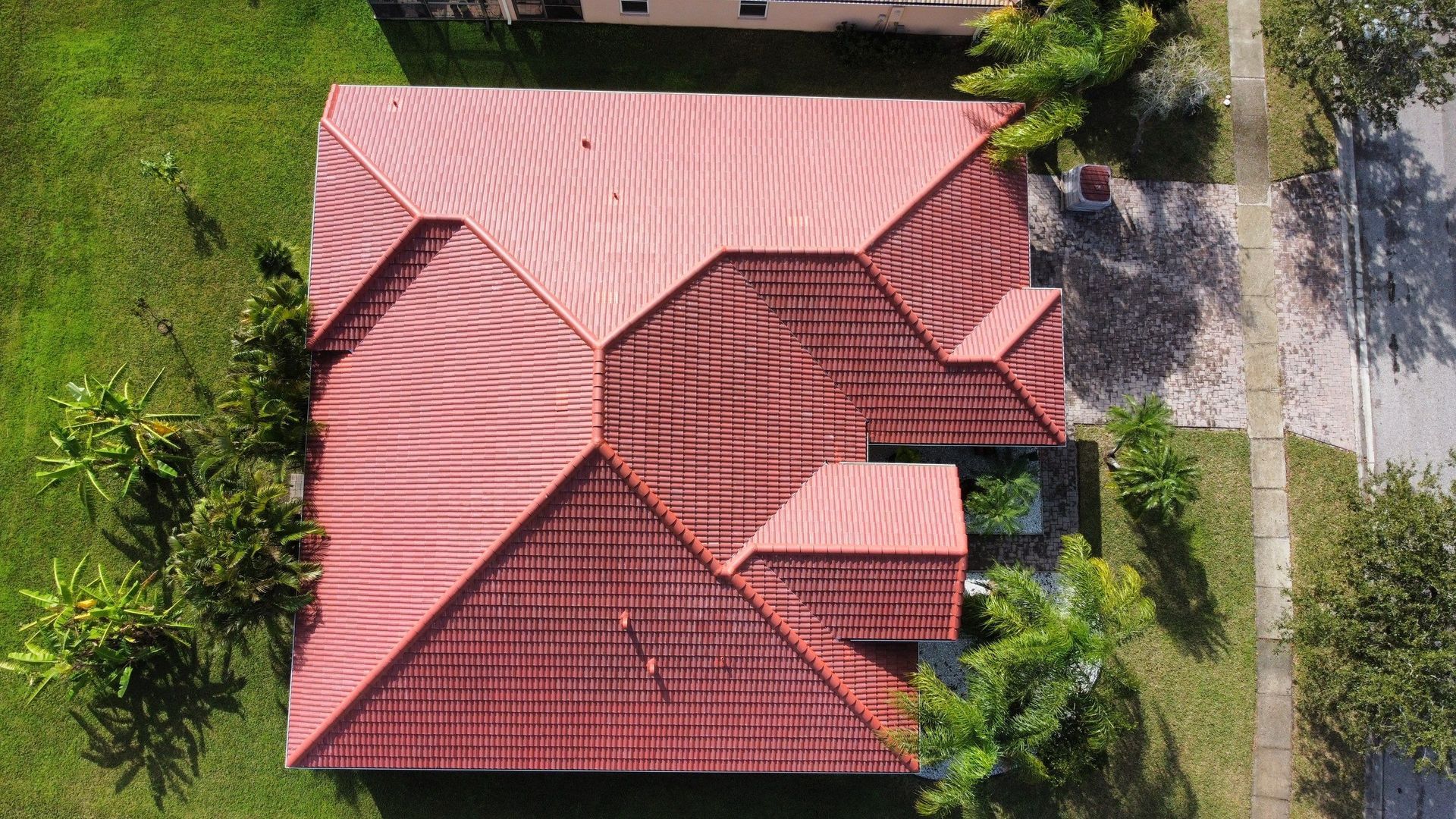 An aerial view of a house with a red tile roof surrounded by trees and grass.