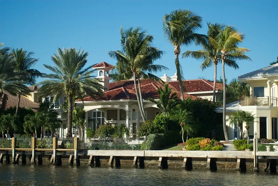 A large house sits next to a body of water surrounded by palm trees