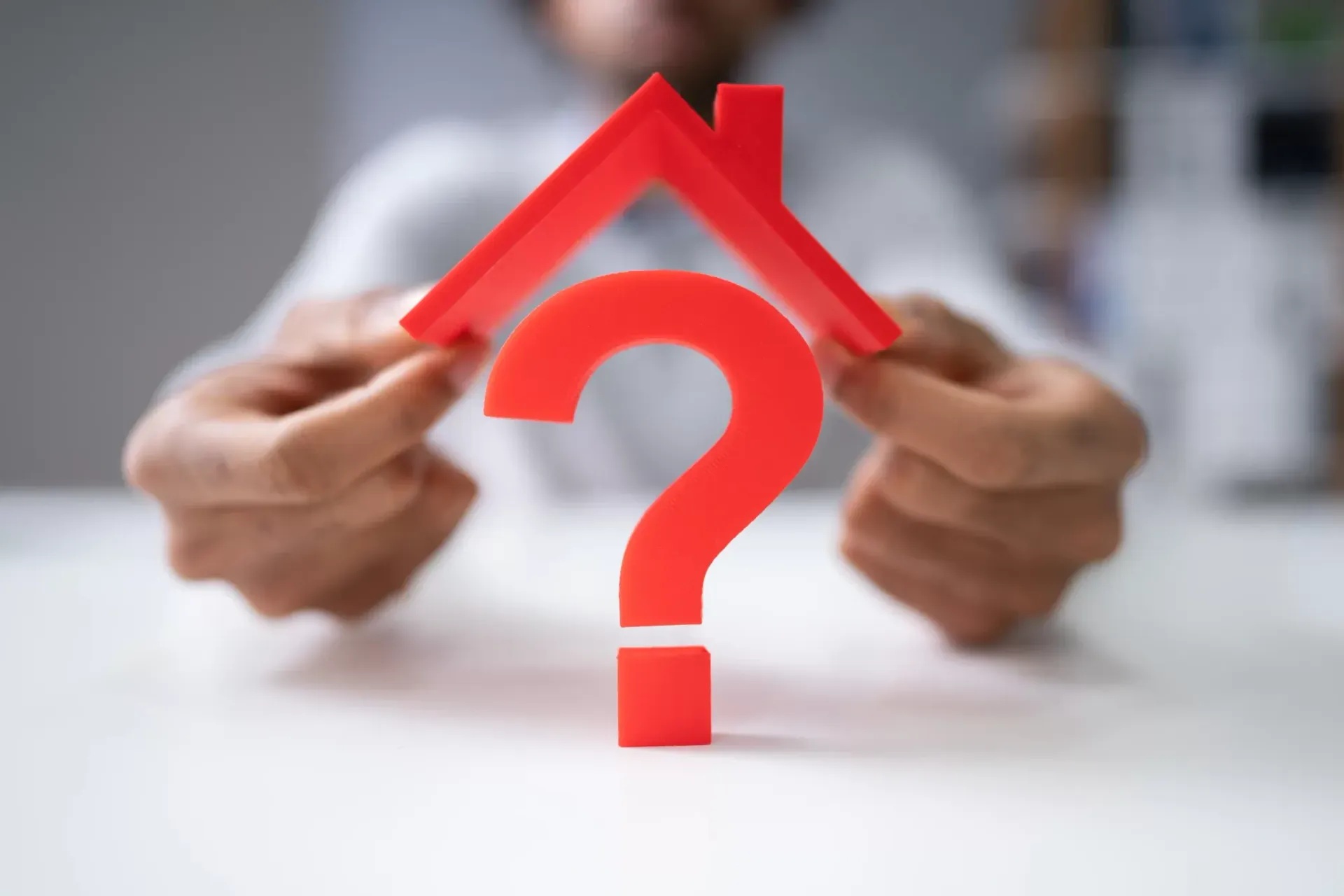 A man is holding a red question mark in the shape of a house.