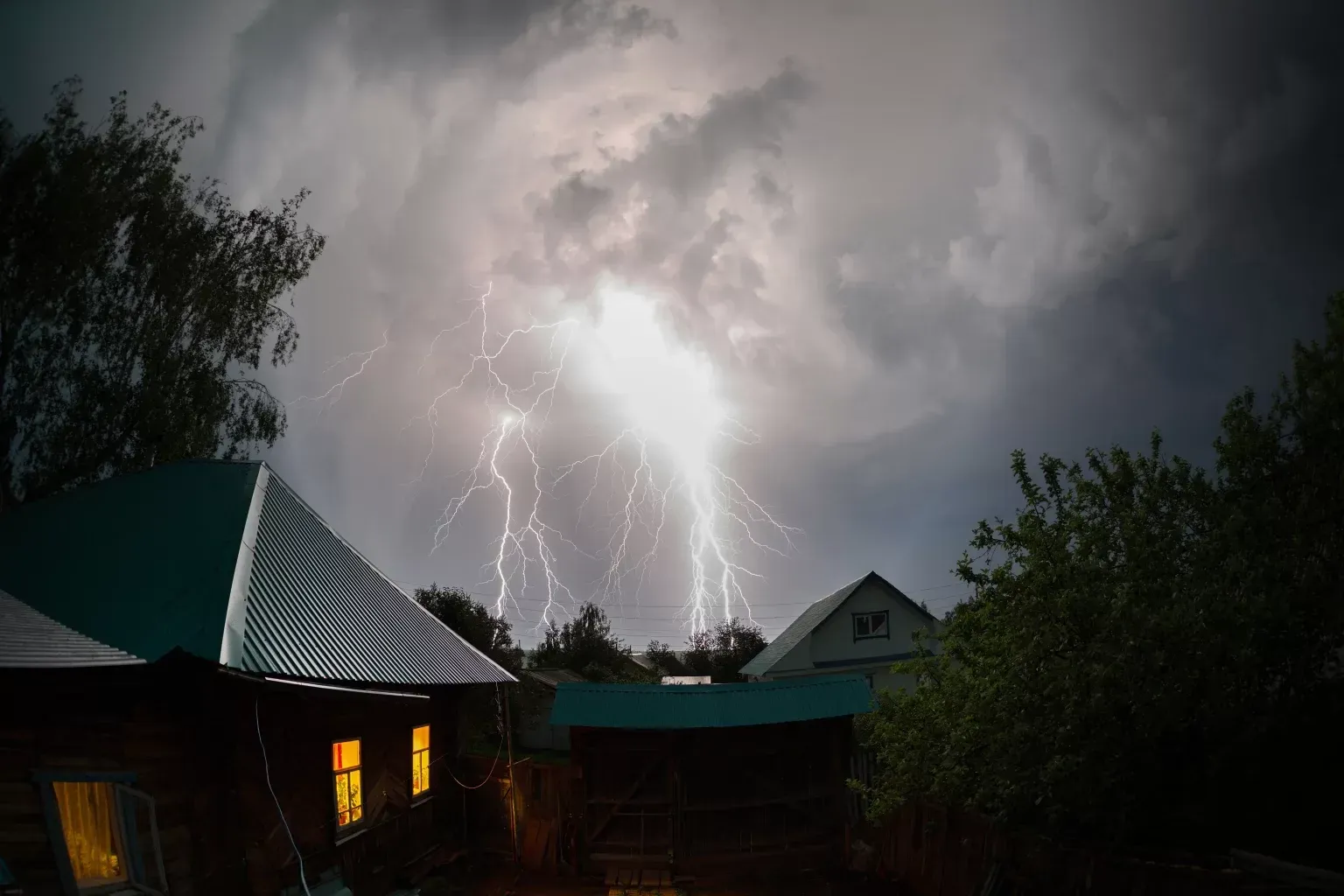 There is a lightning storm in the sky over a house.