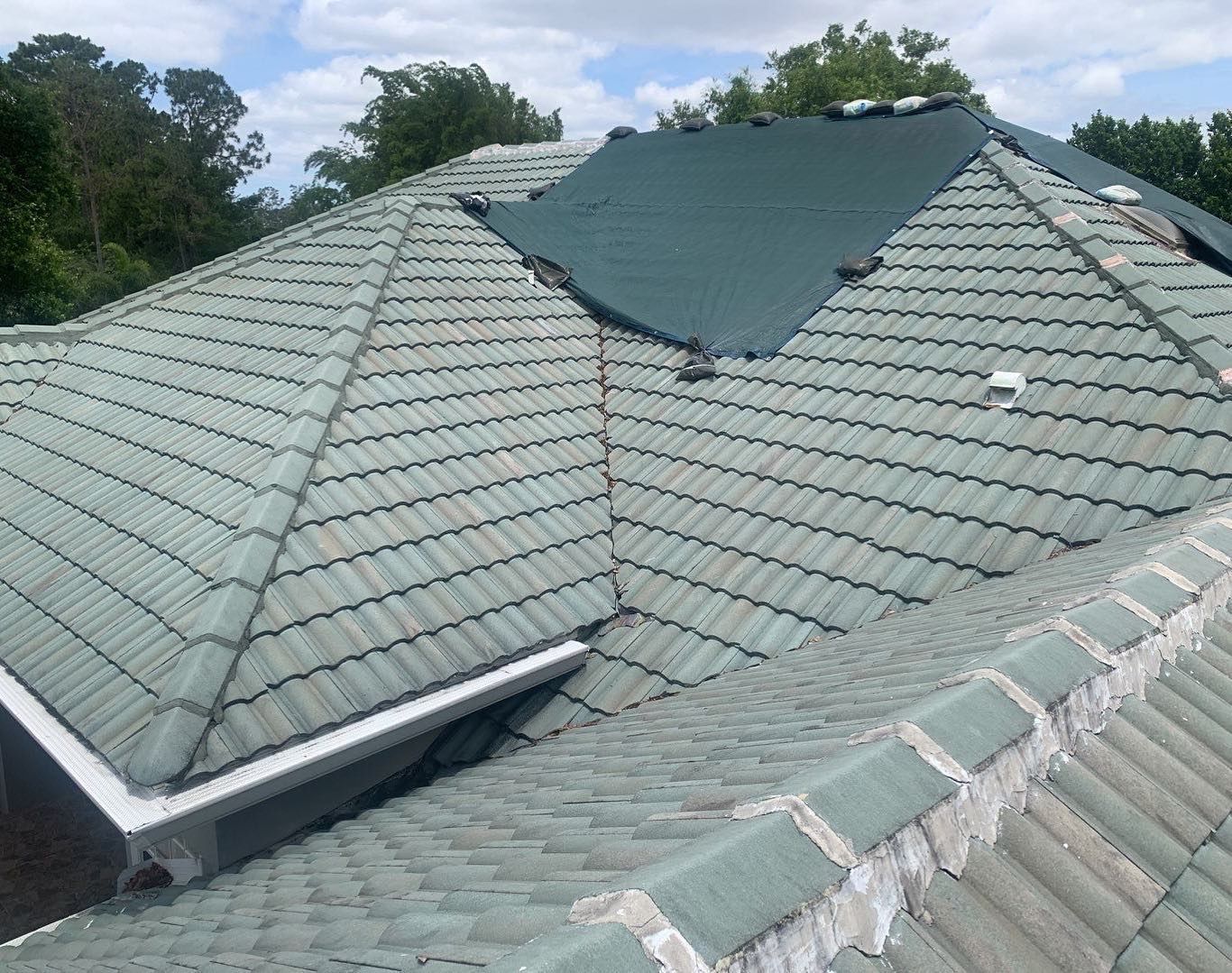 The roof of a house with a green tile roof and trees in the background.