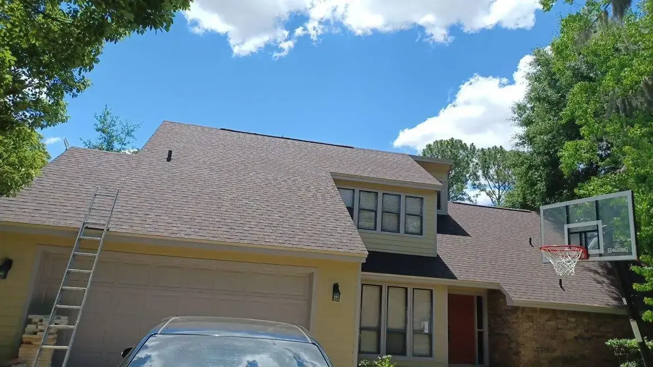 A car is parked in front of a house with a ladder on the roof.