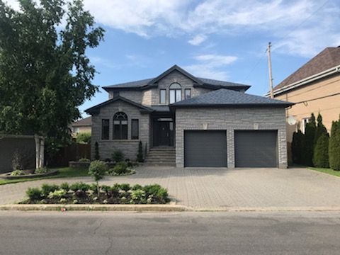 Une grande maison avec deux portes de garage se trouve au bord de la route.