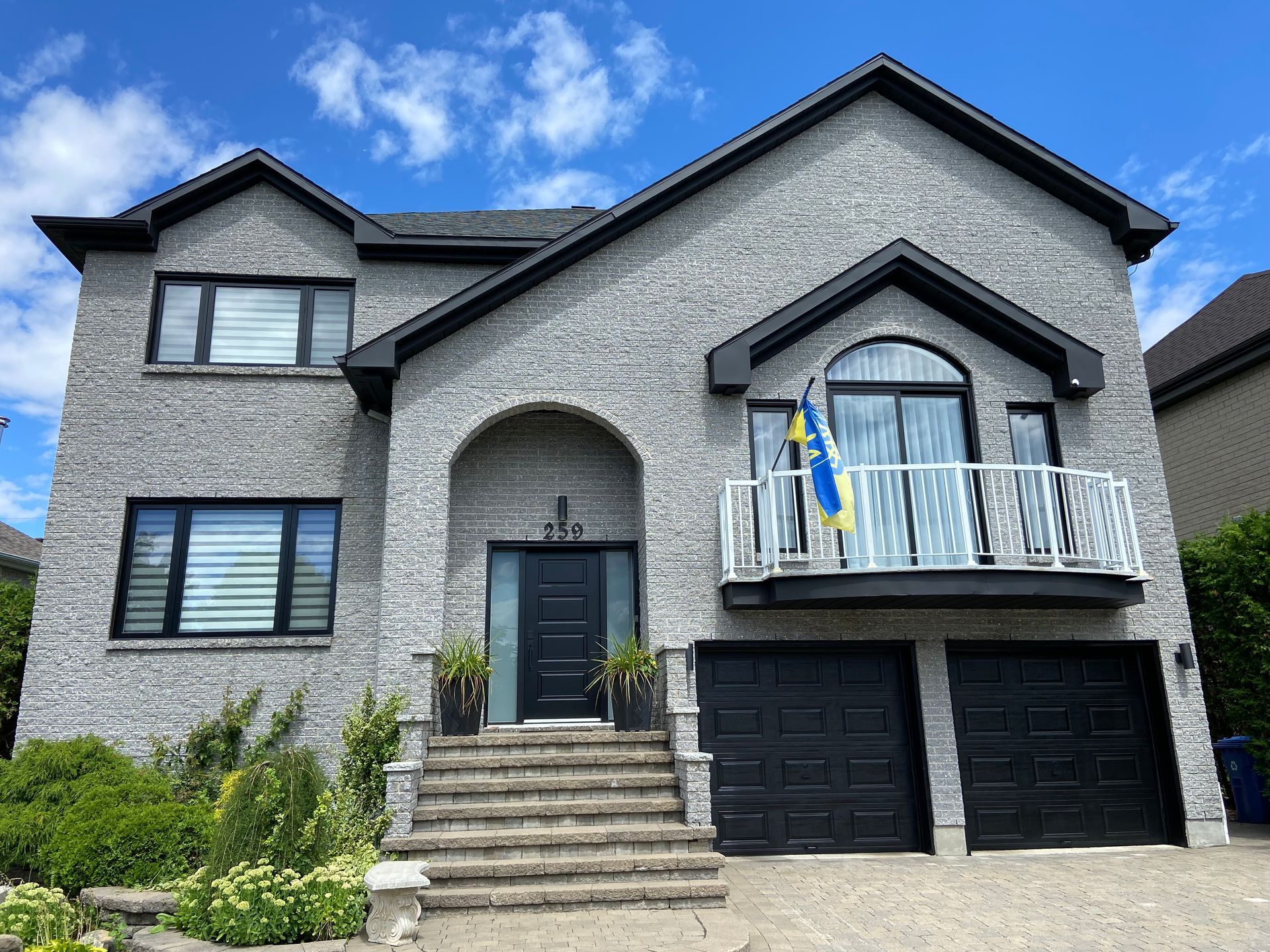 Une grande maison en brique avec des portes de garage noires et un balcon.