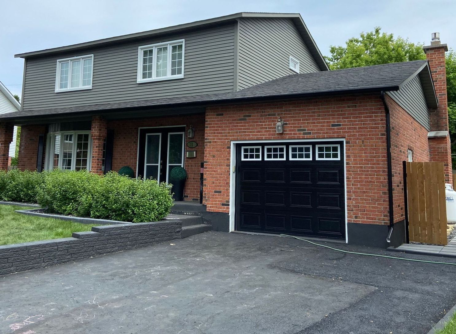 Une maison en brique avec une porte de garage noire et une allée.