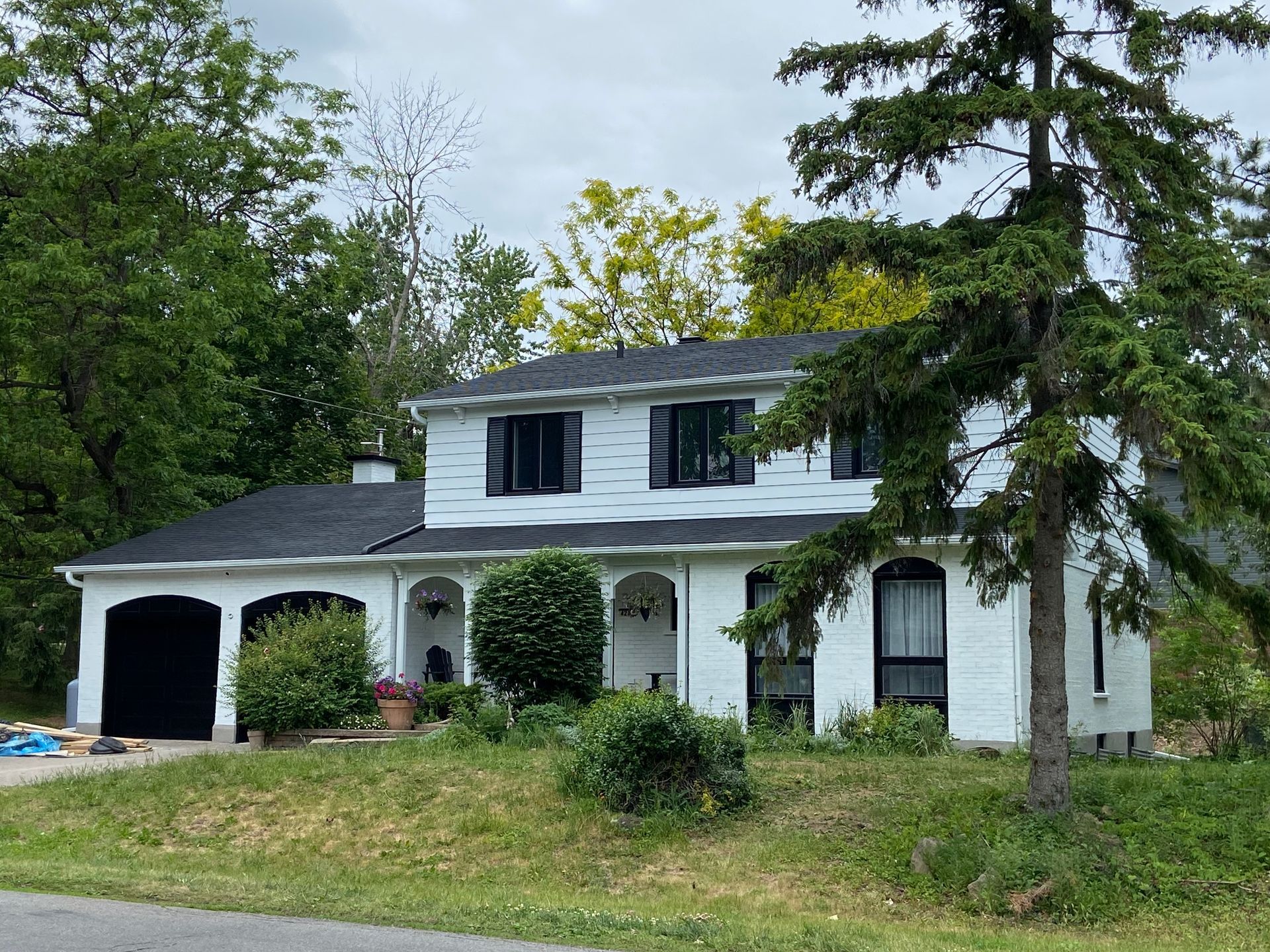 Une maison blanche au toit noir est entourée d'arbres.