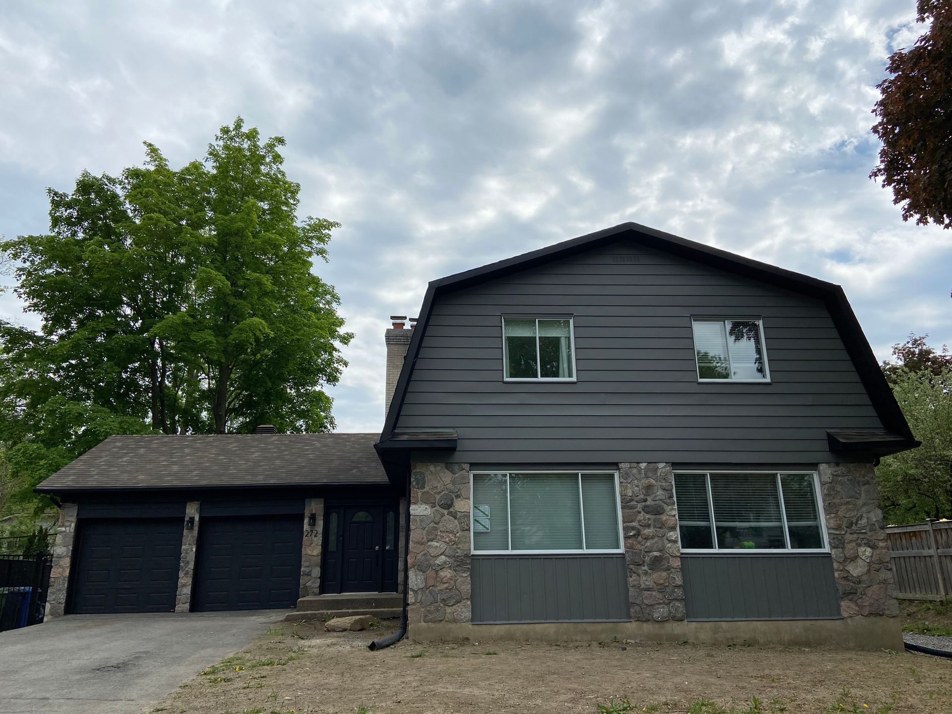 Une grande maison avec un bardage gris et une porte de garage noire