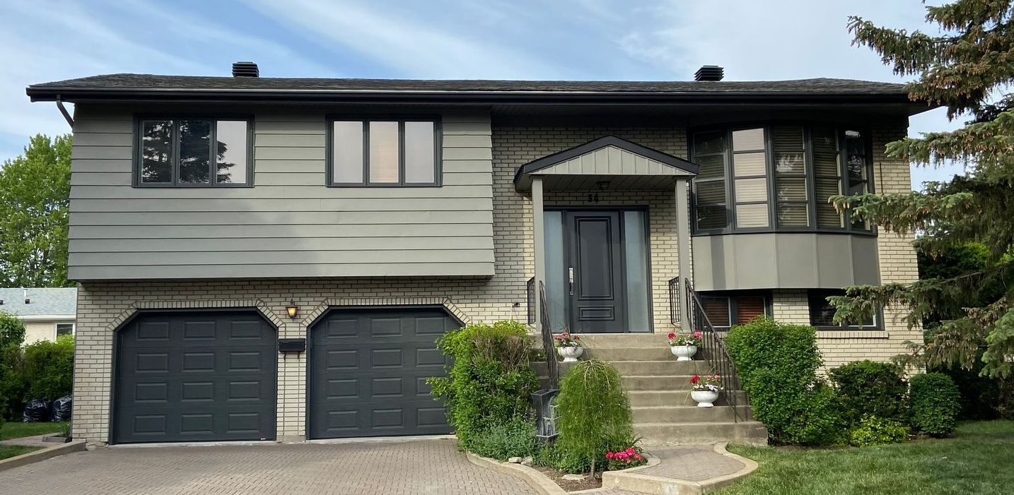 Une grande maison en brique avec deux portes de garage noires et des escaliers qui y mènent.