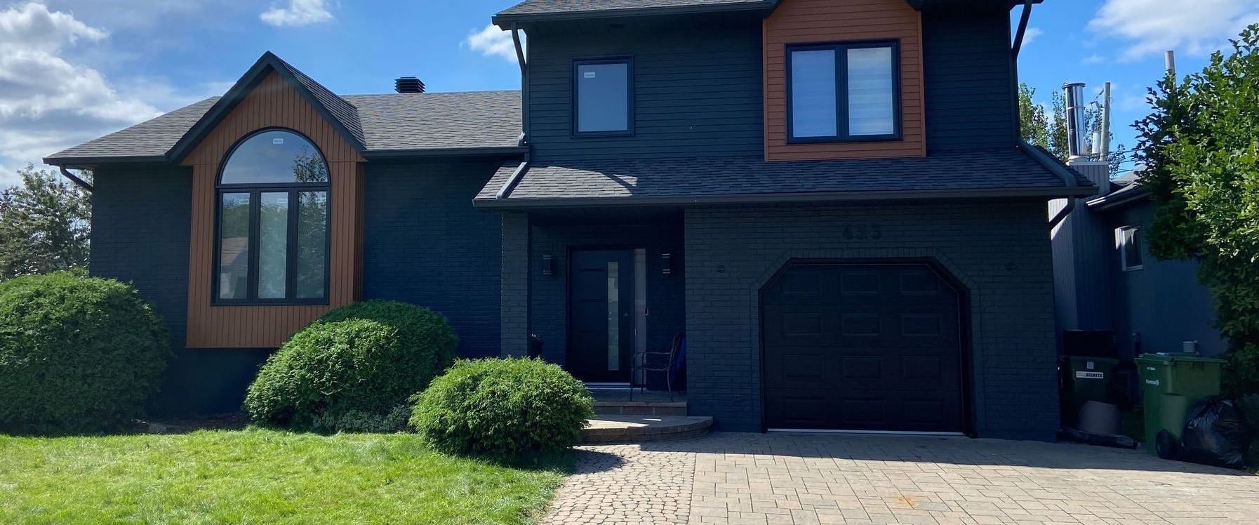 Une maison noire avec un garage et une allée devant.